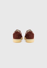 Brune nubuck sko med lav profil, som har en beige gummisål og enkel søm ved hælen. Rund tå-design.