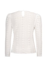Witte blouse met lange mouwen, voorzien van een gestructureerd kantontwerp, een sleutelgat aan de achterkant en ingewikkelde diamant- en bloemenpatronen doorheen.