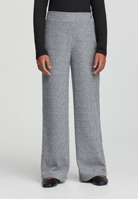 Szare spodnie o szerokich nogawkach z prążkowanej tkaniny, z elastycznym pasem i miękkim dzianinowym materiałem, w komplecie z czarnym obuwiem.