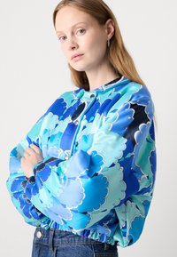 Giacca bomber blu con motivo floreale, con chiusura a zip, polsini arricciati e orlo elastico, realizzata in tessuto leggero e lucido.