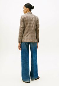 Blazer à carreaux marron avec des lignes d'accent claires, associé à un jean denim bleu à jambes larges avec un ourlet effiloché, vu de dos.