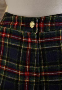 Vilnas maisījuma rūtainas bikses ar tumši zilu, zaļu, sarkanu un dzeltenu rakstu, zelta pogas aizdari un teksturētu virsmu.