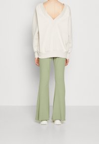 Light beige V-neck sweatshirt with open back, paired with flared, ribbed, light green pants and white sneakers.