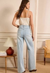 Lichtblauwe wijde jeans met hoge taille, met achterzakken en een ontspannen pasvorm. Gekocht met een crèmekleurige satijnen top en platformhakken.