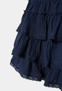 Jupe bleu marine à volants avec taille élastique, présentant un tissu froncé et une bordure en dentelle festonnée sur chaque couche à volants.