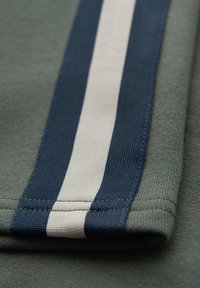 Close-up of green fabric with a thick navy stripe and a thinner white stripe running parallel along the edge, showing stitching detail.