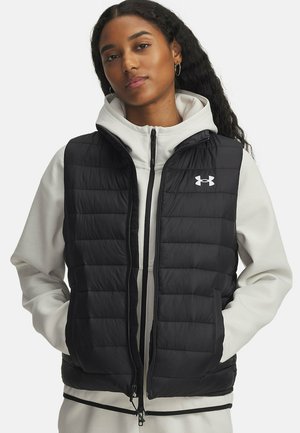 Schwarze Steppweste mit durchgestepptem Design, frontalem Reißverschluss und Seitentaschen. Enthält ein weißes Under Armour-Logo auf der linken Brust. Über einem hellen Hoodie getragen.