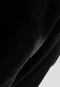 Tessuto nero con una morbida texture vellutata; la luce si riflette sottilmente sulla superficie, rivelando contorni e pieghe lisci.