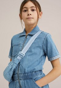 Denimov kombinezon svetlo modre barve s kratkimi rokavi, zadrgo spredaj in žepom na prsih; vključuje ujemajočo svetlo modro torbico preko telesa z nastavljivim trakom.