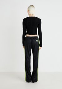 Melnā garām piedurknēm tops ar teksturētu audumu, apvienots ar melniem biksēm ar laima zaļām sānu svītrām un logo detaļu aizmugurē.