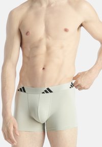 Světlé šedé boxerky s černým páskem s logem Adidas. Vyrobené z měkké tkaniny, s přiléhavým střihem a konturovanou kapsou.