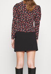 Blouse noire et rouge à fleurs avec manches bouffantes, coupe ajustée, tissu texturé, associée à une jupe noire simple.