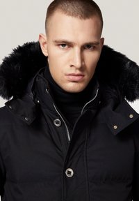 Czarna pikowana kurtka z kapturem wyłożonym futrem, z suwakiem, napami i wysokim kołnierzem. Miękka tekstura i elegancki design.