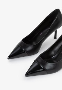 Décolleté neri in pelle con tacco alto, caratterizzati da una punta affusolata, una tomaia liscia e un accento lucido sulla punta. Design minimalista con un tacco sottile.