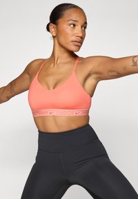 Koralni sportski grudnjak s tankim trakama i širokim remenom s "Nike Sportswear" brendiranjem, kombiniran s crnim tajicama visokog struka.