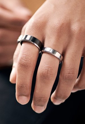 To metallringer, en med en matt finish og den andre polert, sitter på fingre med en naturlig hudtekstur. Minimalistisk design. Sølvfarge.