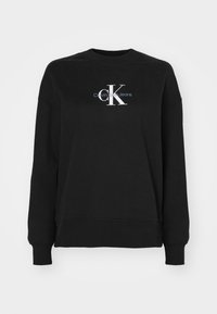 Črna dukserica iz bombažne mešanice, s krojaškim ovratnikom in dolgimi rokavi. Spredaj je prikazan bel in moder logotip Calvin Klein Jeans.