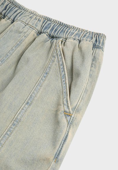 Pantalon en denim bleu clair avec une ceinture élastique et des coutures visibles de poche latérale sur un fond uni.