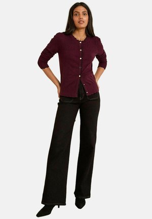 Cardigan en tricot bordeaux avec un col festonné et une fermeture par boutons, associé à un pantalon noir à jambes larges et des escarpins noirs à bouts pointus.