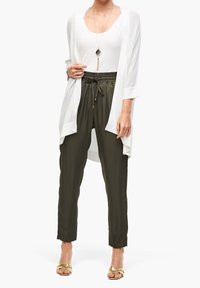 Bílý lehký kardigan přes bílý top, doplněný olivově zelenými zúženými kalhotami s elastickým pasem a zlatými sandály.