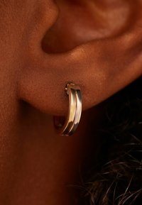 Gouden en zilveren oorbel met een slank ontwerp met twee parallelle metalen banden, die een gepolijste textuur en een ronde vorm tonen.