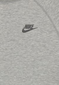 Sivi materijal s crnim Nike logotipom i swooshom otisnutim blizu izreza, prikazuje teksturirane šavove duž ramena.