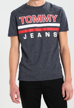 Ciemnoszary bawełniany t-shirt z dużym czerwono-białym napisem „TOMMY JEANS” na piersi. Klasyczny okrągły dekolt i krótkie rękawy.