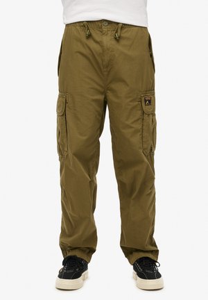 Pantalons cargo vert olive avec ceinture ajustable, plusieurs poches sur les côtés et poignets élastiques aux chevilles. Portés avec des baskets noires.