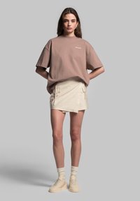 Brun oversized t-shirt, beige teksturerede shorts med sidelukke, og lysfarvede platform sneakers, parret med hvide sokker.