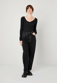 Crna dugodlana V-izrez majica u kombinaciji s visokim strukom, širokim crnim trapericama. Odjeća ima teksturiranu tkaninu i jednostavan dizajn. Crne čizme do gležnja upotpunjuju izgled.