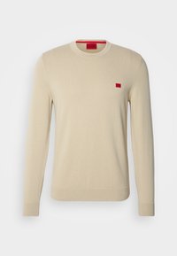 Beige Strickpullover mit rundem Halsausschnitt und langen Ärmeln. Verfügt über ein kleines rotes Logo auf der linken Brust sowie gerippte Bündchen und Saum.