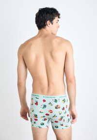 Boxershorts i lyseblå med et fruktmønster, med en grønn midjebånd med "BJÖRN BORG"-merke. Glatt stoff og tettsittende design.