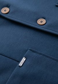 Mörkblått tyg med två träknappar och en sydd ficka som har en liten metalltagg med texten "Ombre Dept."