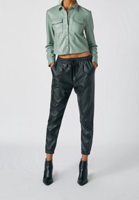 Chemise en cuir vert menthe coupée, avec deux poches poitrine, associée à des joggers en simili cuir noirs dotés d'une taille et de poignets élastiques.