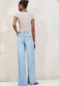 Jeans de pierna ancha color azul claro con cintura alta, cuentan con dos bolsillos traseros y una etiqueta de color claro. Combinados con una camiseta ajustada beige.