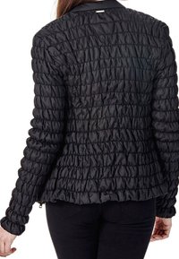 Giacca nera trapuntata con una texture arricciata, maniche lunghe e un design aderente. Presenta un colletto e una piccola etichetta decorativa sul retro.