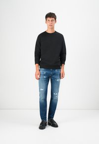 Black sweatshirt with round neckline, paired with light blue distressed jeans featuring rips and dark shoes. Simple and casual design.