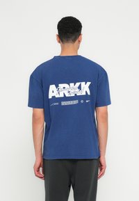 Navy plava pamučna majica kratkih rukava s velikim bijelim natpisom na leđima koji glasi "ARKK Innovations Included."