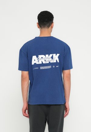 Navy plava pamučna majica kratkih rukava s velikim bijelim natpisom na leđima koji glasi "ARKK Innovations Included."