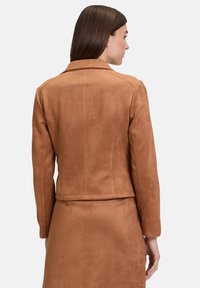 Brown faux suede jacket with a slim fit, featuring a notch collar and smooth texture. The back is plain with a cropped cut that matches a skirt.
