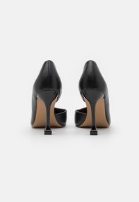 Chaussures à talons hauts en cuir noir avec un bout pointu et un talon aiguille incliné, présentant une surface lisse et un design minimaliste.