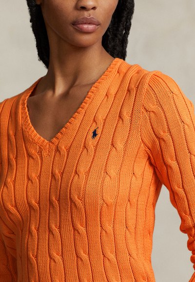 Pull en V en tricot torsadé de couleur orange vif, avec une texture côtelée et un petit emblème bleu sur la poitrine.