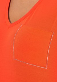 Oranges V-Ausschnitt-T-Shirt mit kurzen Ärmeln, ausgestattet mit einer einzelnen Tasche, die am Rand mit Strasssteinen verziert ist. Glatte Textur.
