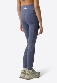 Lilla høytlivsstrømpebukser med sidelomme, glatt tekstur og reflekslogo på linningen, kombinert med lette tursko.