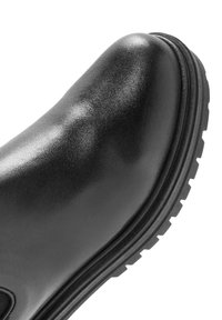 Czarny skórzany but z gładką, błyszczącą teksturą, okrągłym noskiem i grubą gumową podeszwą z głębokimi wzorami bieżnika zapewniającymi przyczepność.