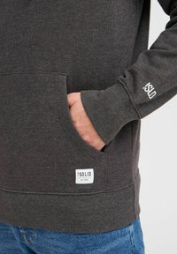 Grijze sweatshirt met een kangoeroe pocket, geribbelde cuffs en een opvallende logo patch. Zachte textuur, casual ontwerp en aangesloten bij de taille.