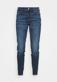 Slim-fit mörkblå denimjeans med framknapp och fickor, visade mot en enfärgad vit bakgrund.