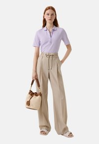 Poloshirt in licht lavendel met een kraag en vier knopen, gecombineerd met high-waisted beige broek en een geweven beige tas met bruine accenten.