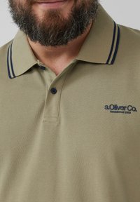Khaki polo shirt met een gestructureerde stof, marineblauwe strepen op de kraag, twee knopen en een klein s.Oliver-logo op de linkerkant van de borst.