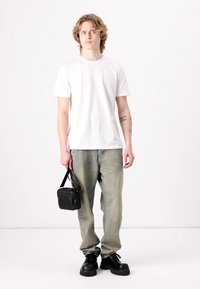 T-shirt di cotone bianco, jeans in denim verde sbiadito, scarpe nere chunky con lacci e una piccola borsa nera. Il modello si trova davanti a uno sfondo neutro.